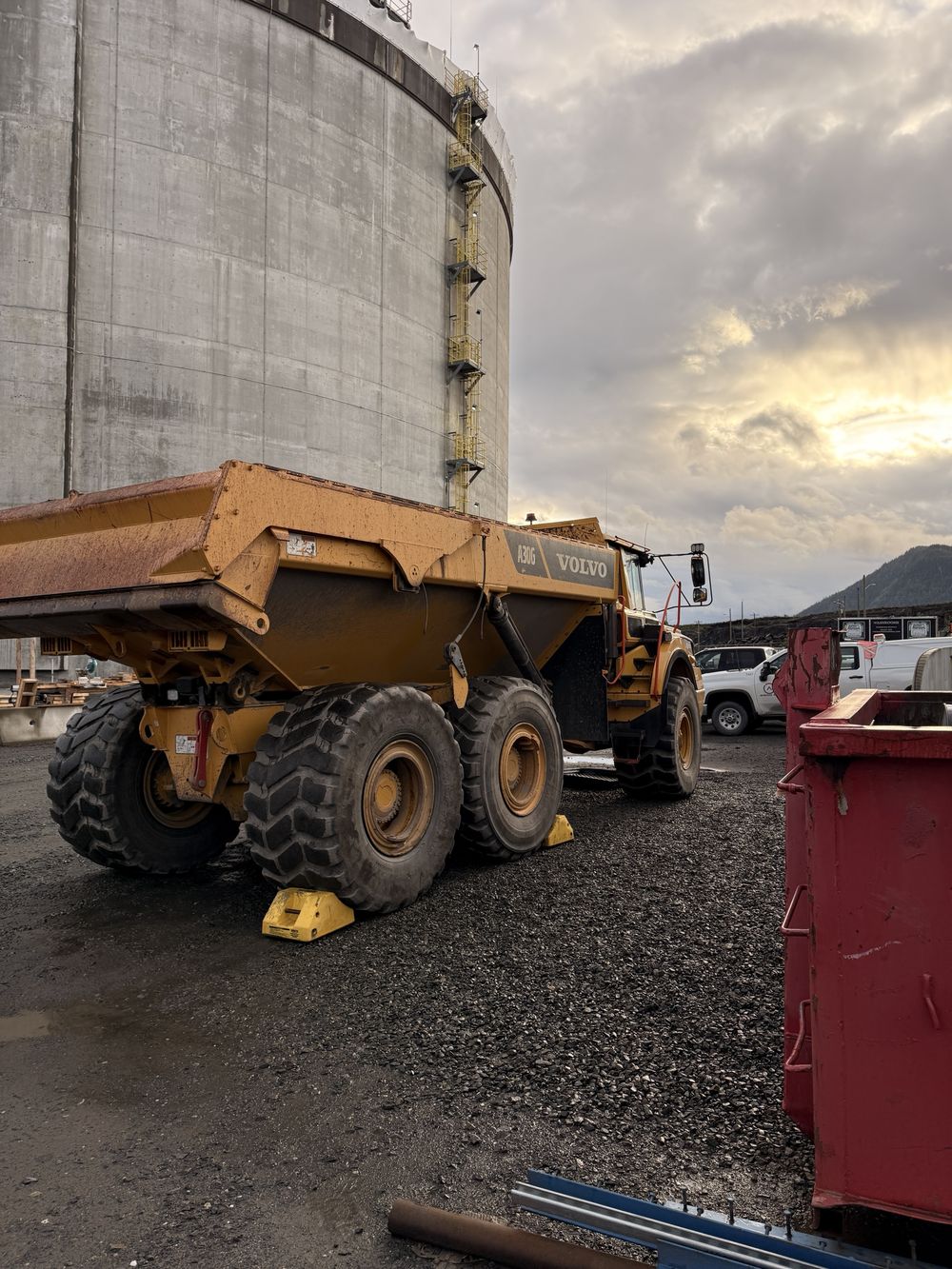 An articulated haul truck parked beside a large concrete storage tank on an industrial site
