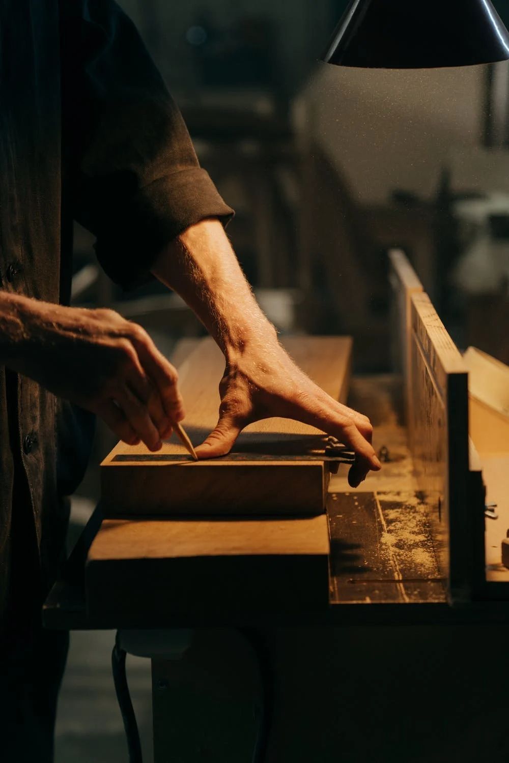 A carpenter marking a board with a pencil on a workshop bench