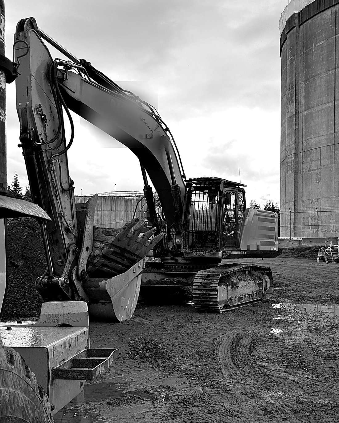 Excavator on an active job site positioned beside a large concrete storage tank
