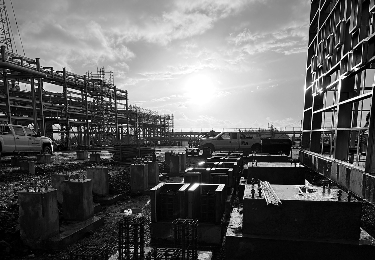 Wide view of an active industrial construction site at sunrise, with structural steel, concrete piers, and site vehicles